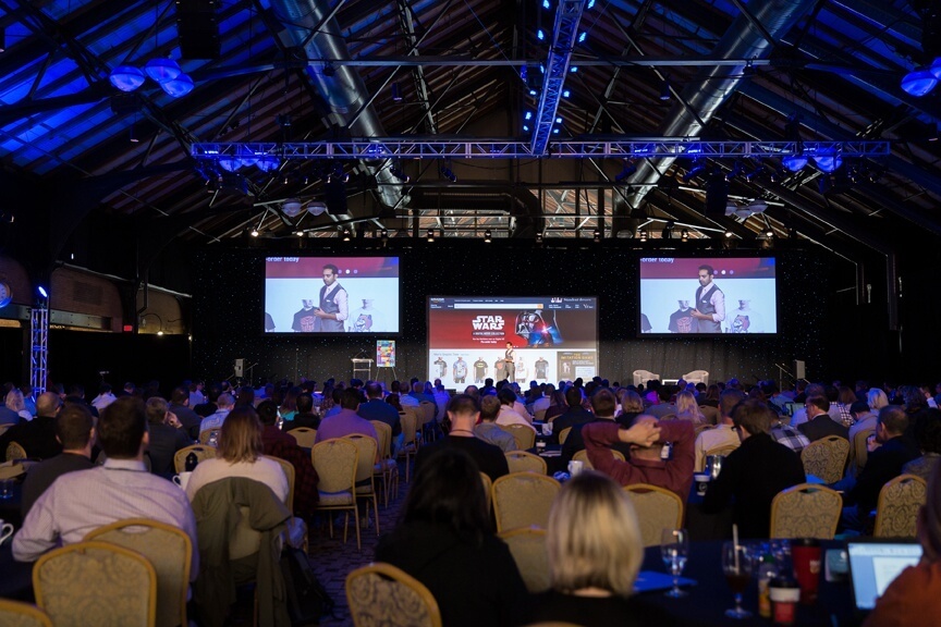 The Converted 2015 conference, with hundreds of people sitting at round tables watching Pat on stage with three screens behind him.