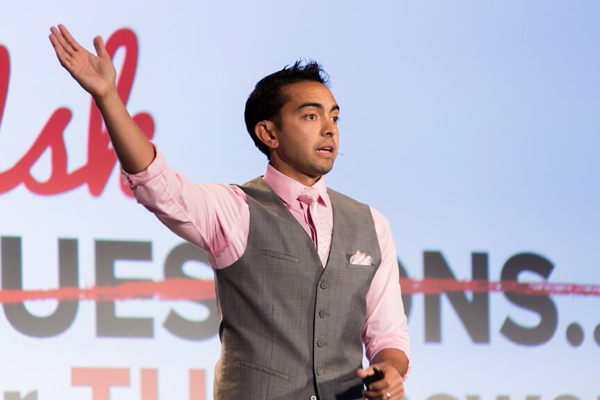 Pat speaking on stage at Converted 2015, wearing a pink button down shirt, pink tie, and gray pants and suit vest.