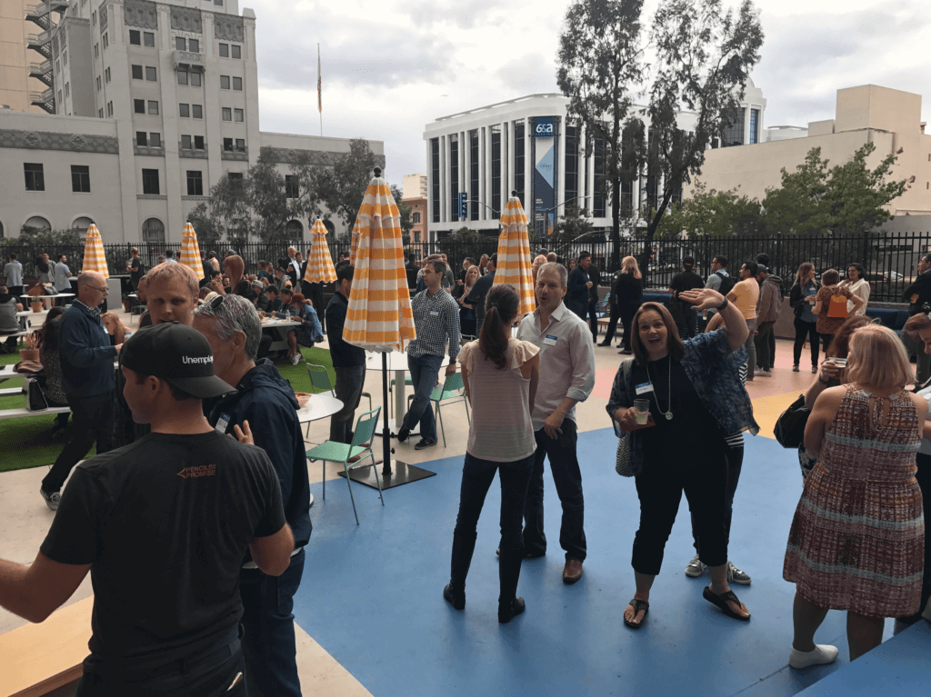 People mingling at a conference on an outdoor terrace. One person is waving.