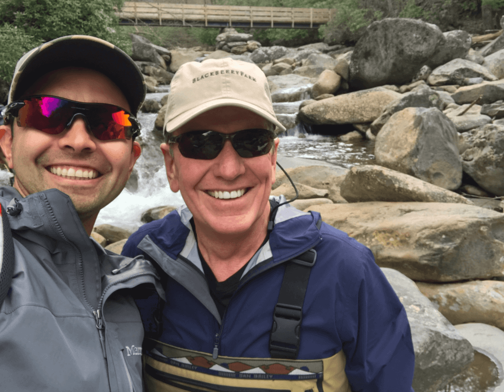 A picture of Pat and Michael dressed in fishing gear, standing in front of a stream