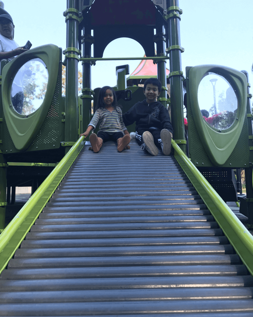 Photo of Pat's two kids sitting on the green slide. They are much bigger in this picture.