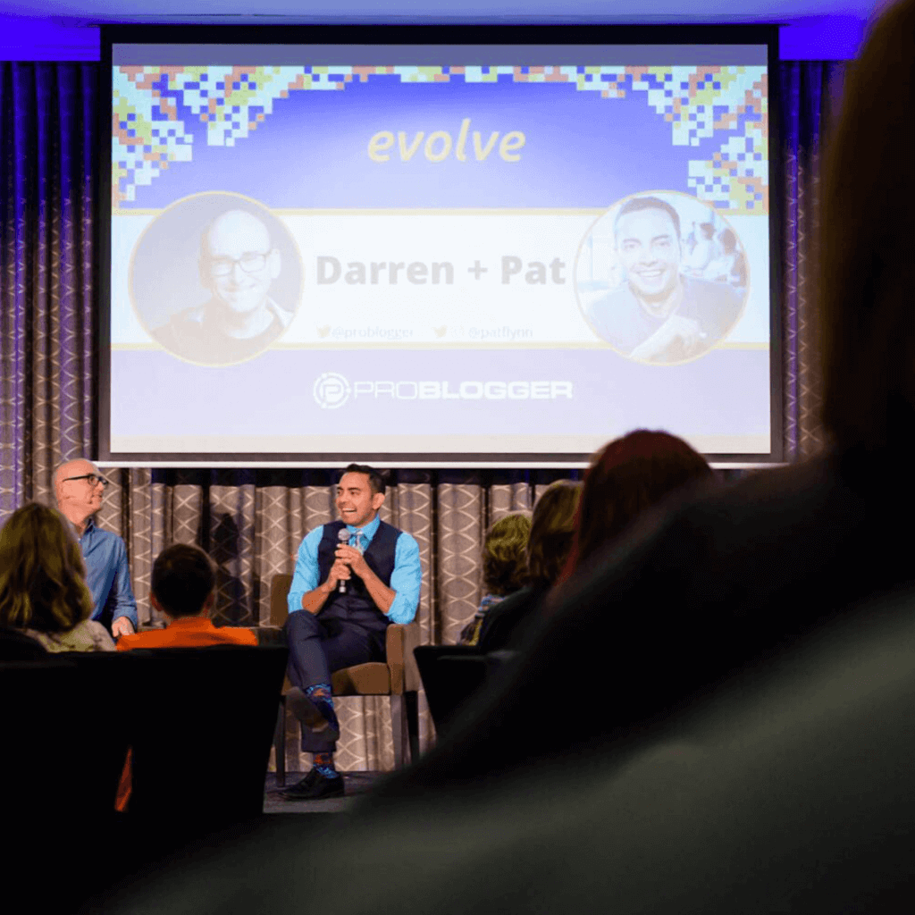 Photo of Darren Rowse and Pat Flynn sitting on a stage underneath a large slide with the conference name, Evolve, and their headshots