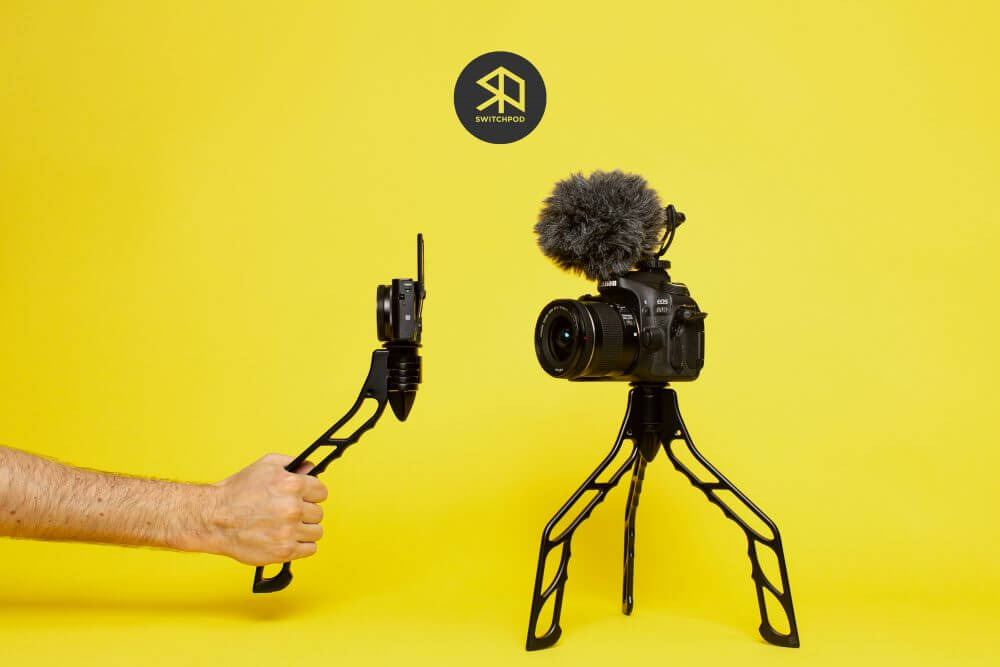 Promotional photo for the SwitchPod, showing the camera tripod both collapsed and being held in video blogging mode and expanded, holding up a camera on its own