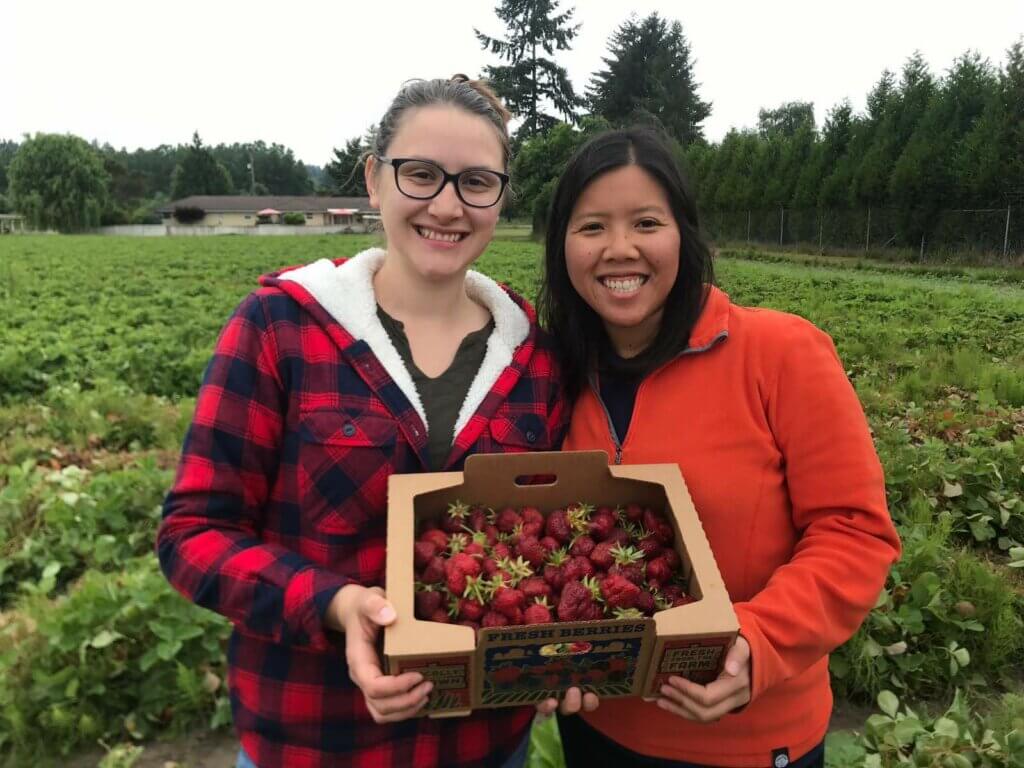 Nalin and her partner, Anna, posing in a field with a big box of strawberries