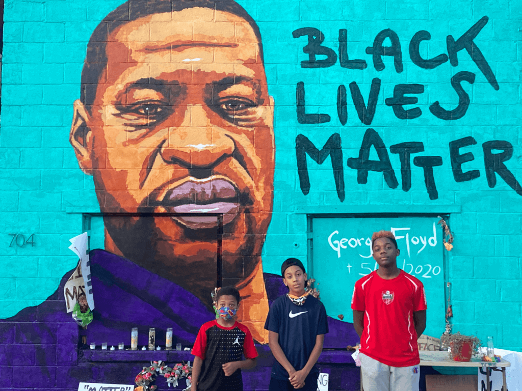 Randy's three boys posing in front of a large mural tribute to George Floyd