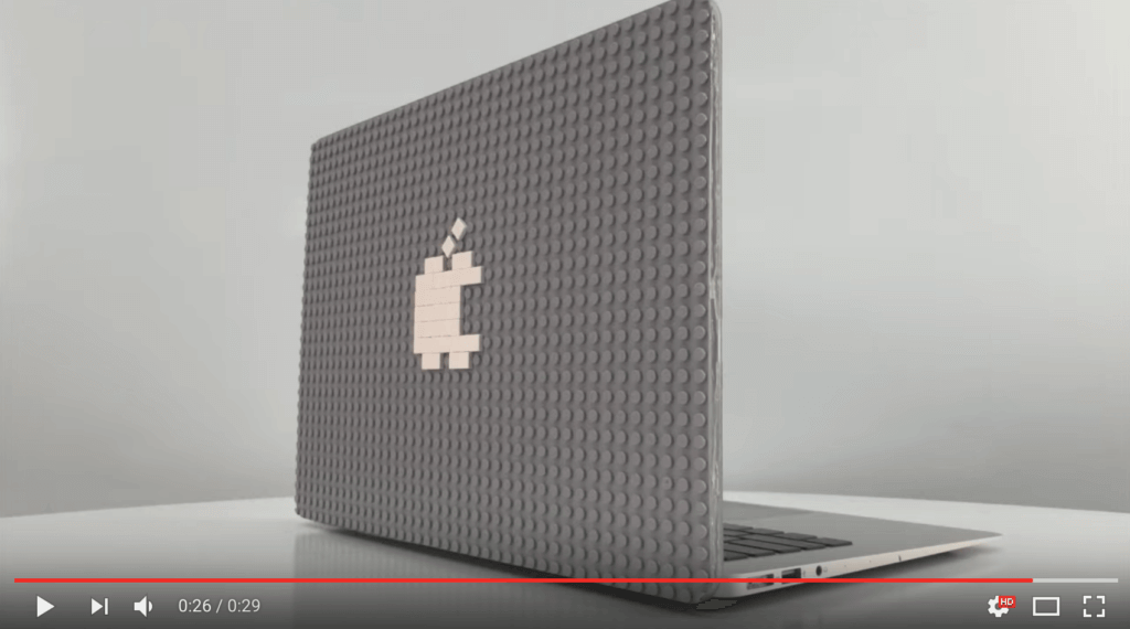 Screenshot of the video, showing a Macbook with a grey Brik Book case with a white Apple logo apple. The video has played 26 of 29 seconds.