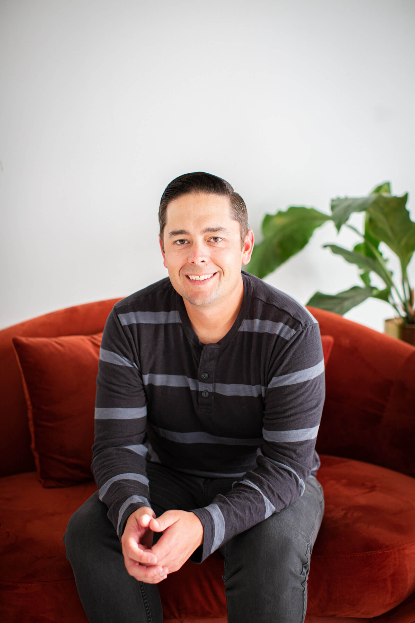 Headshot of Jeremy Launder, smiling, sitting on a red chair