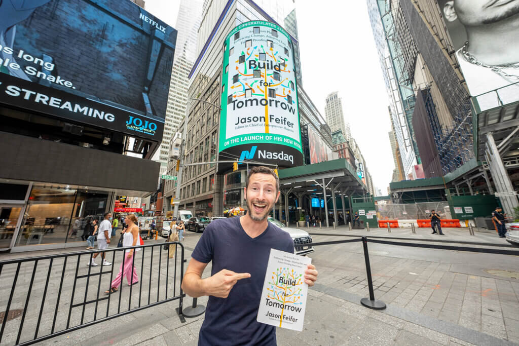 Jason posing with his book "Build for Tomorrow" in front of a huge billboard