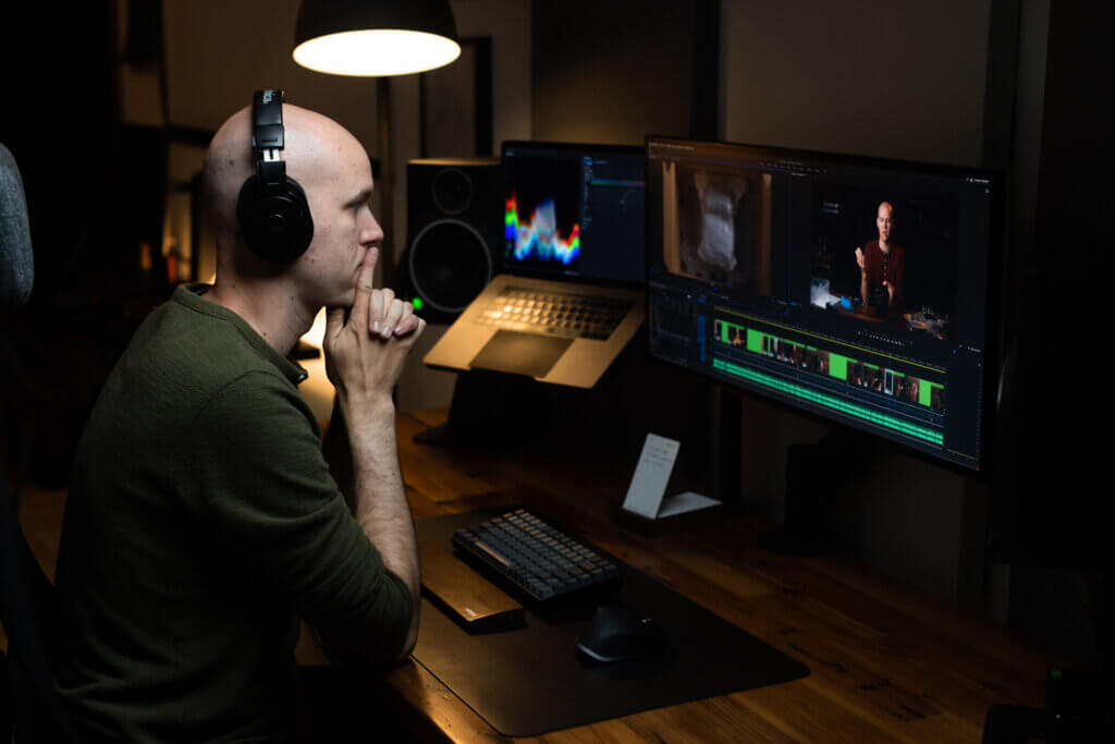 SPI Expert in Residence Caleb Wojcik sits at his workstation with headphones in, watching footage via video editing software.