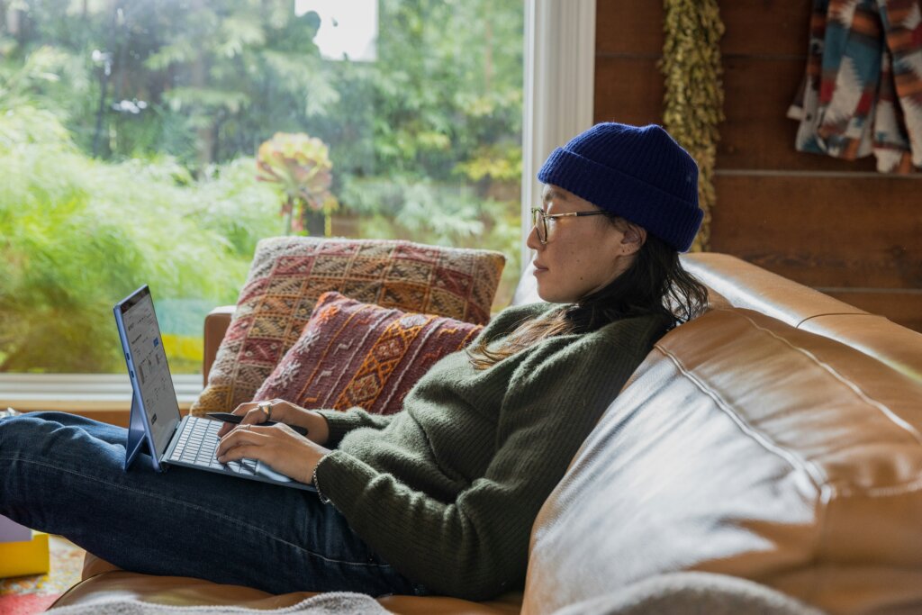A woman sits on a leather couch, working on her Microsoft Edge.