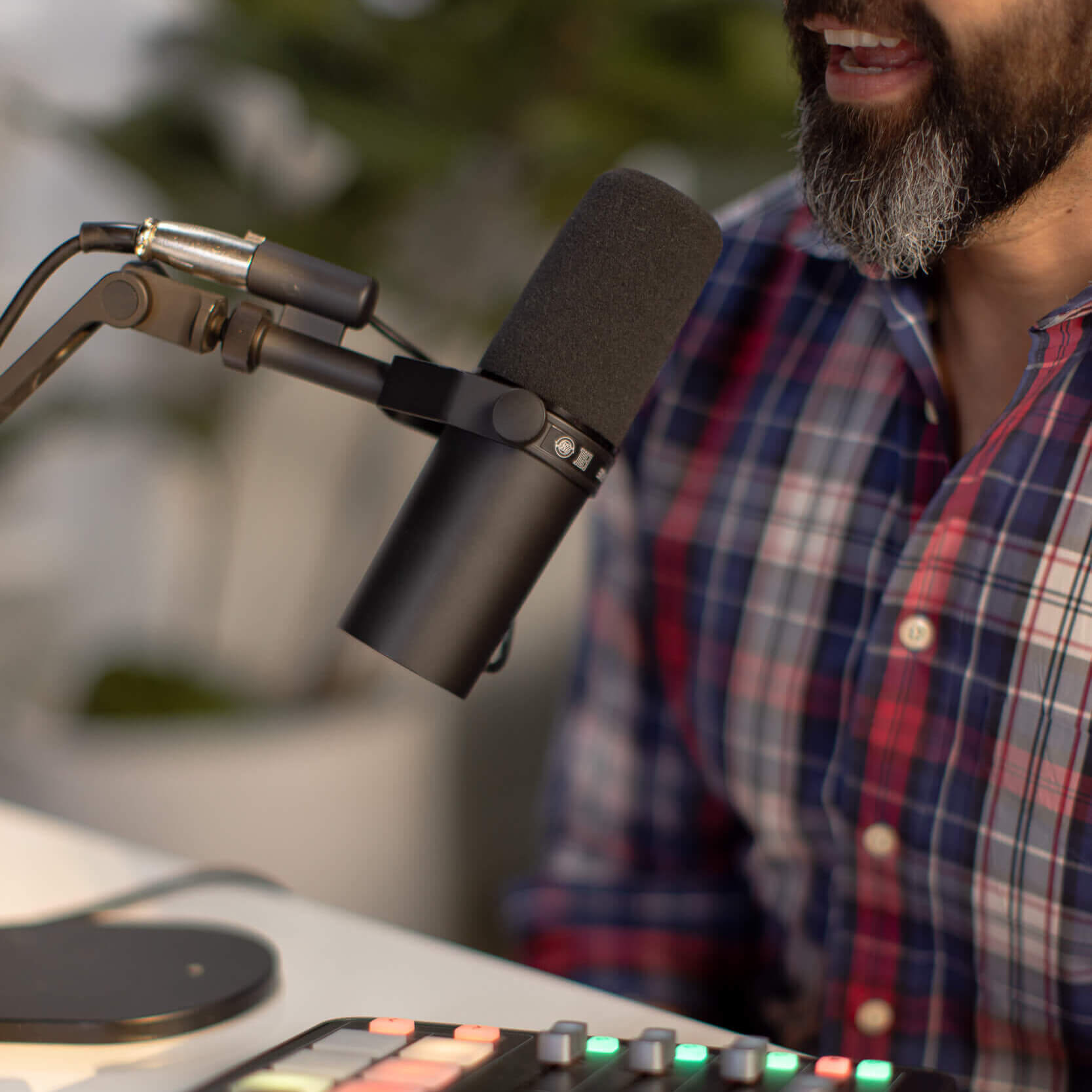 Talking into a podcast microphone with a control board on the desk